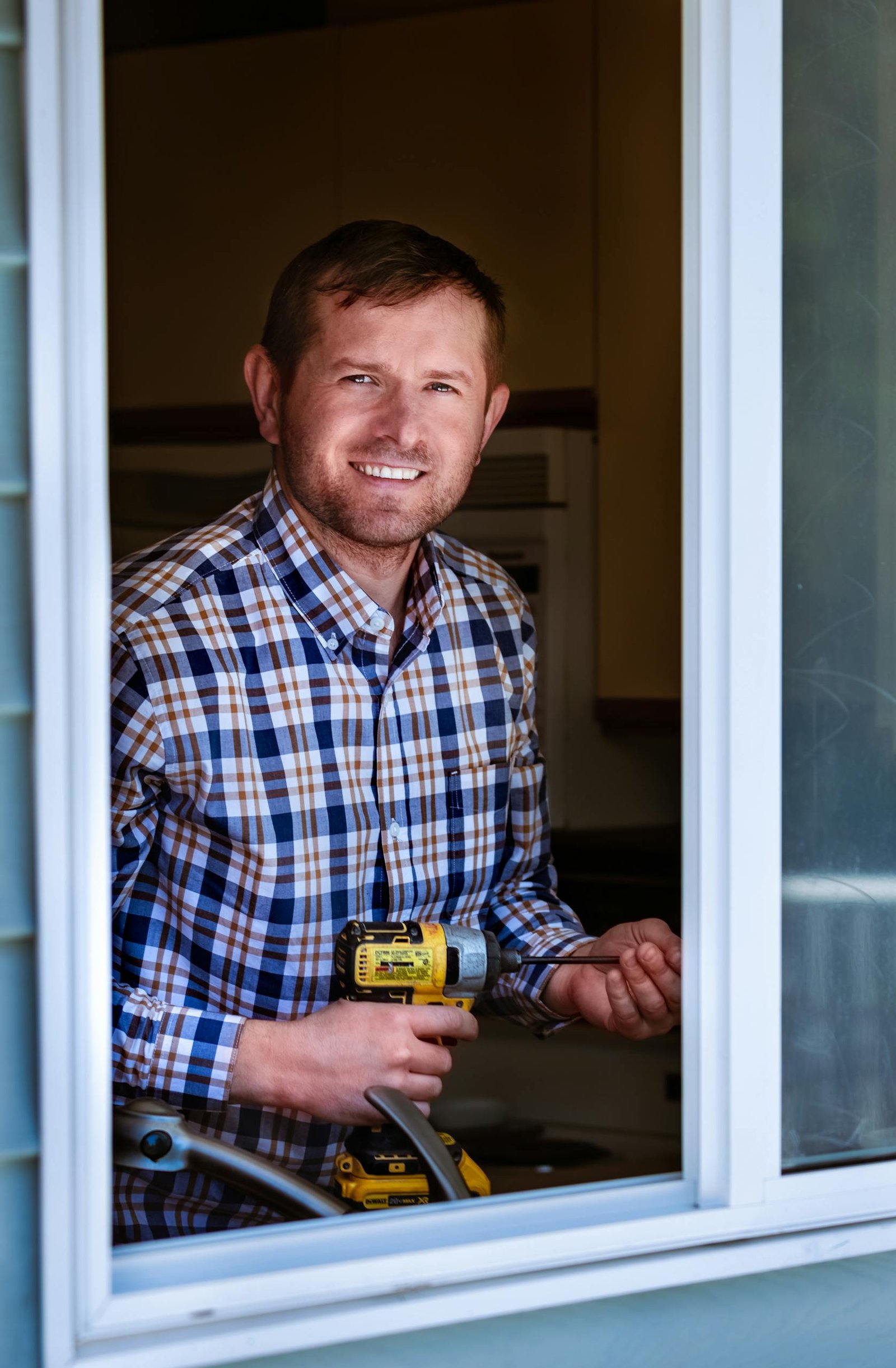 A young worker in Nanaimo, BC, smiling while holding a drill, seen through a window.